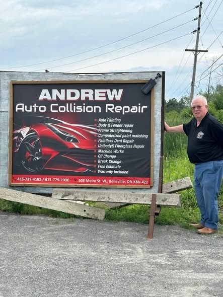 A man standing beside the Andrew Auto Collision Repair roadside sign