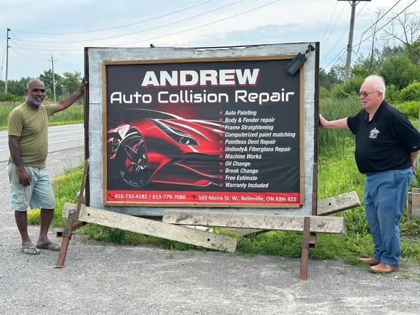 Two people standing at the Andrew Auto Collision Repair roadside sign